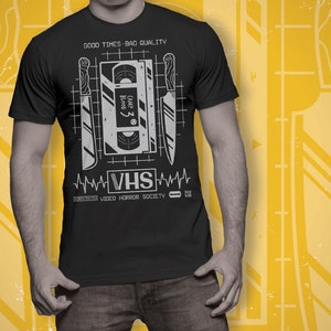 May include: Black t-shirt with a graphic of a VHS tape and knives. The text "GOOD TIMES BAD QUALITY" and "VHS VIDEO HORROR SOCIETY" is printed on the shirt.