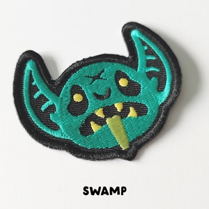 Pu&ograve; includere: Toppa ricamata verde e gialla di un mostro dei cartoni animati con la scritta "SWAMP" sotto.