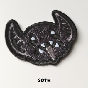 Pu&ograve; includere: Toppa da stirare ricamata nera di un pipistrello dei cartoni animati con occhi e denti bianchi. La toppa dice "GOTH" in basso.