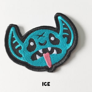 Pu&ograve; includere: Un toppa ricamata blu e nera di un mostro dei cartoni animati con la lingua rosa che sporge. Il mostro ha grandi orecchie e un ampio sorriso. Il testo "ICE" &egrave; stampato sotto la toppa.
