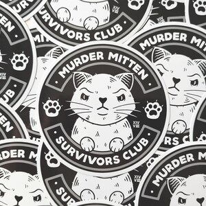 Pu&ograve; includere: Primo piano di diversi adesivi rotondi in bianco e nero con un'illustrazione di un gatto dei cartoni animati e il testo "Murder Mitten Survivors Club".