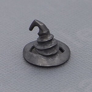 May include: A small, silver-colored, witch's hat charm with a pointed top and a spiral design. The hat is sitting on a round base.
