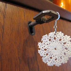 May include: A white crocheted doily earring hanging from a keyhole in a wooden door.