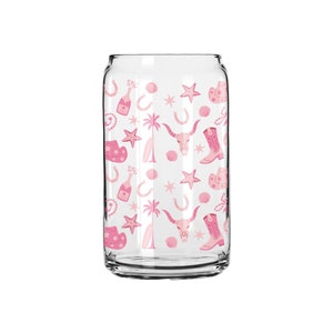 May include: A clear glass can with a pink and white pattern of cowboy boots, stars, horseshoes, and palm trees.