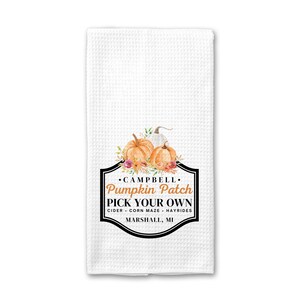May include: White kitchen towel with a black and white graphic of pumpkins and flowers. The graphic says "Campbell Pumpkin Patch Pick Your Own Cider - Corn Maze - Hayrides Marshall, MI"