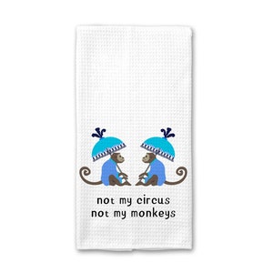May include: White kitchen towel with two monkeys wearing blue jackets and holding blue umbrellas. The text "not my circus not my monkeys" is printed below the monkeys.
