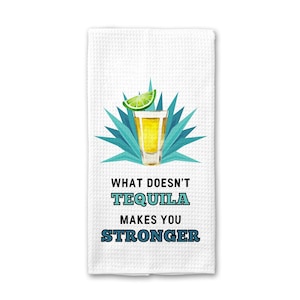 May include: White kitchen towel with a blue and green agave plant and a shot glass of tequila with a lime wedge. The text reads "What doesn't tequila make you stronger."