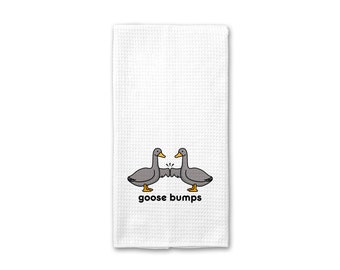 Könnte beinhalten: Ein weißes Küchentuch mit zwei Cartoon-Graugänsen, die sich mit ausgebreiteten Flügeln gegenüberstehen. Der Text "goose bumps" ist unter den Gänsen gedruckt.