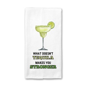 May include: White kitchen towel with a green lime wedge and a glass of green tequila. The text on the towel reads "What doesn't tequila make you stronger."
