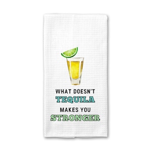 May include: White kitchen towel with a green lime wedge and a shot glass of tequila. The text reads "What doesn't tequila makes you stronger".