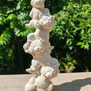 May include: A cream-colored cat sculpture featuring five stacked cats. The cats are in various poses, creating a whimsical and playful design. The sculpture is made of a textured material and stands on a wooden surface.