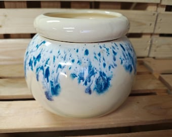 May include: A ceramic jar with a lid, featuring a cream-colored base and a striking blue splatter design. The jar has a rounded shape and a wide opening, suitable for storage or decorative purposes. The lid is a matching cream color.