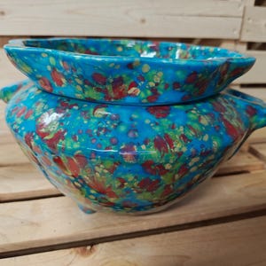 May include: A two-piece ceramic planter set. The pieces are glazed in a vibrant turquoise with a speckled pattern of red, green, and yellow. The bottom piece is a rounded bowl with three small feet and handles.