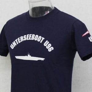 May include: A navy blue t-shirt featuring a white silhouette of a submarine and the text "U-BOOT U96" in a white arc above the submarine.