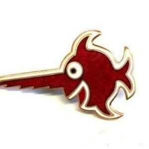 May include: A red and white enamel pin shaped like a stylised fish with a long, saw-toothed snout.