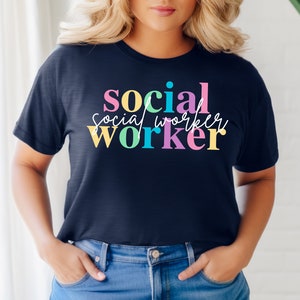 Può includere: Una maglietta blu navy con il testo "social worker" in lettere colorate. Il testo è impilato verticalmente con "social" in rosa e giallo, "worker" in verde e blu, e "social" in scrittura bianca.