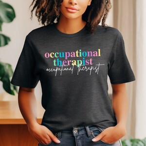 May include: A dark gray t-shirt with the text "occupational therapist" in colorful letters. The text is repeated in a smaller font below the first line.
