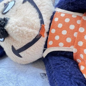 May include: Vintage plush toy with a cream-colored face, black smile, and blue body. The toy has orange polka-dot accents and black and white eye details. A charming, nostalgic collectible.