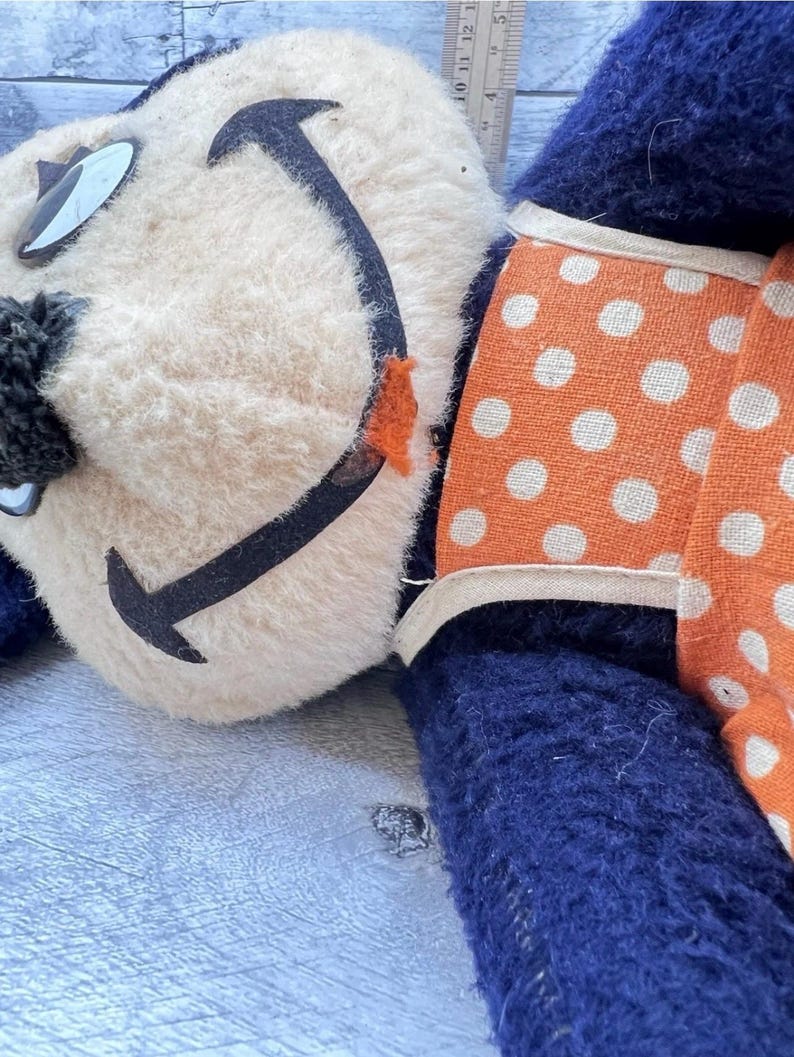 May include: Vintage plush toy with a cream-colored face, black smile, and blue body. The toy has orange polka-dot accents and black and white eye details. A charming, nostalgic collectible.