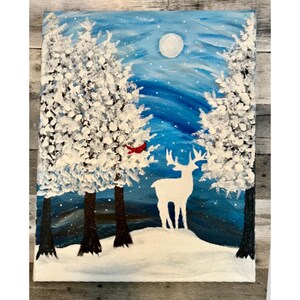 May include: A snowy winter scene with a white deer standing in the foreground. Two snow-covered trees are in the background, with a red cardinal perched on one of the trees. The sky is a deep blue with a full moon and stars.