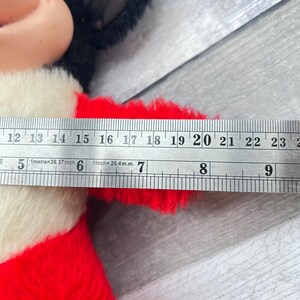 May include: A vintage Mickey Mouse plush toy with black ears, a beige face, and a red and white outfit. The toy's arm measures approximately 18 cm in length, as indicated by a ruler.