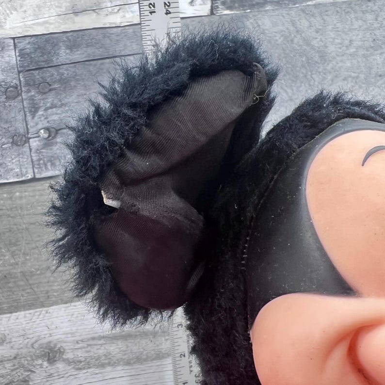 May include: Close-up of a black plush toy ear with a furry trim. The ear is partially visible, revealing a soft, dark interior. A ruler is placed next to the ear for measurement.