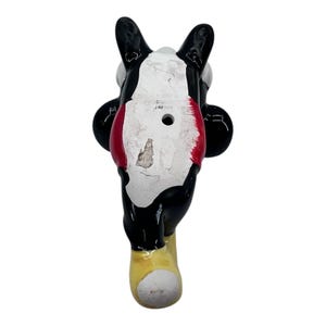 May include: Vintage ceramic figurine of a cartoon character, featuring a black body, white face, and red accents. The figurine has a yellow foot and black ears. The bottom of the figurine has the text "PRODUCE IN JAPAN".