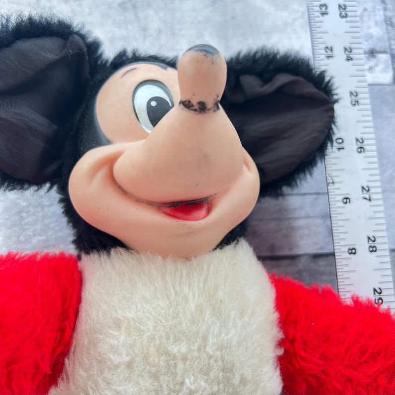 May include: A vintage Mickey Mouse soft toy. The toy has a black head and ears, a pink nose and mouth, and a red and white body. This is a classic Disney character.