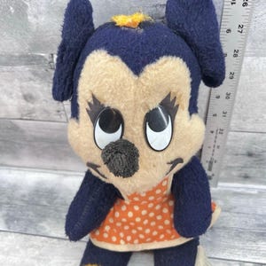 May include: Vintage plush toy featuring a cartoon character with a navy blue head and ears, a tan face, and large black eyes. The character wears an orange dress with white polka dots and yellow accents. The toy is approximately 10 inches tall.