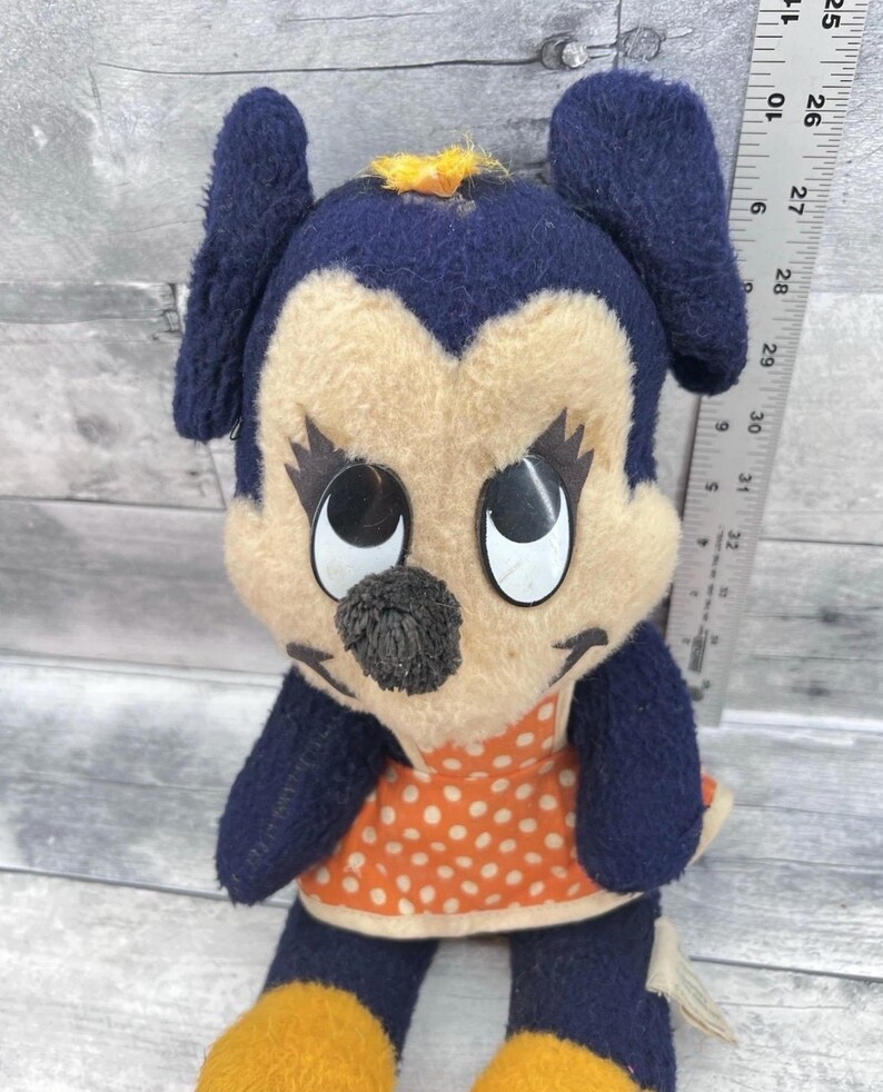 May include: Vintage plush toy featuring a cartoon character with a navy blue head and ears, a tan face, and large black eyes. The character wears an orange dress with white polka dots and yellow accents. The toy is approximately 10 inches tall.