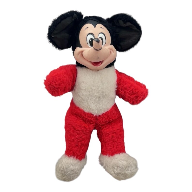 May include: A plush Mickey Mouse toy with a black head and ears, a red body, white chest and feet. The toy has a smiling face with a pink mouth and a white background.