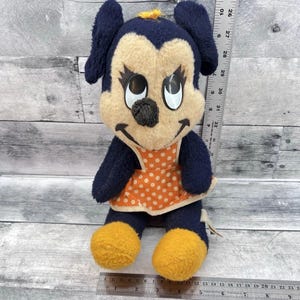 May include: Vintage plush doll featuring a cartoon character with a navy blue head and ears, a tan face, and orange and white polka-dot dress. The doll has yellow feet and a black nose. A ruler is next to the doll.