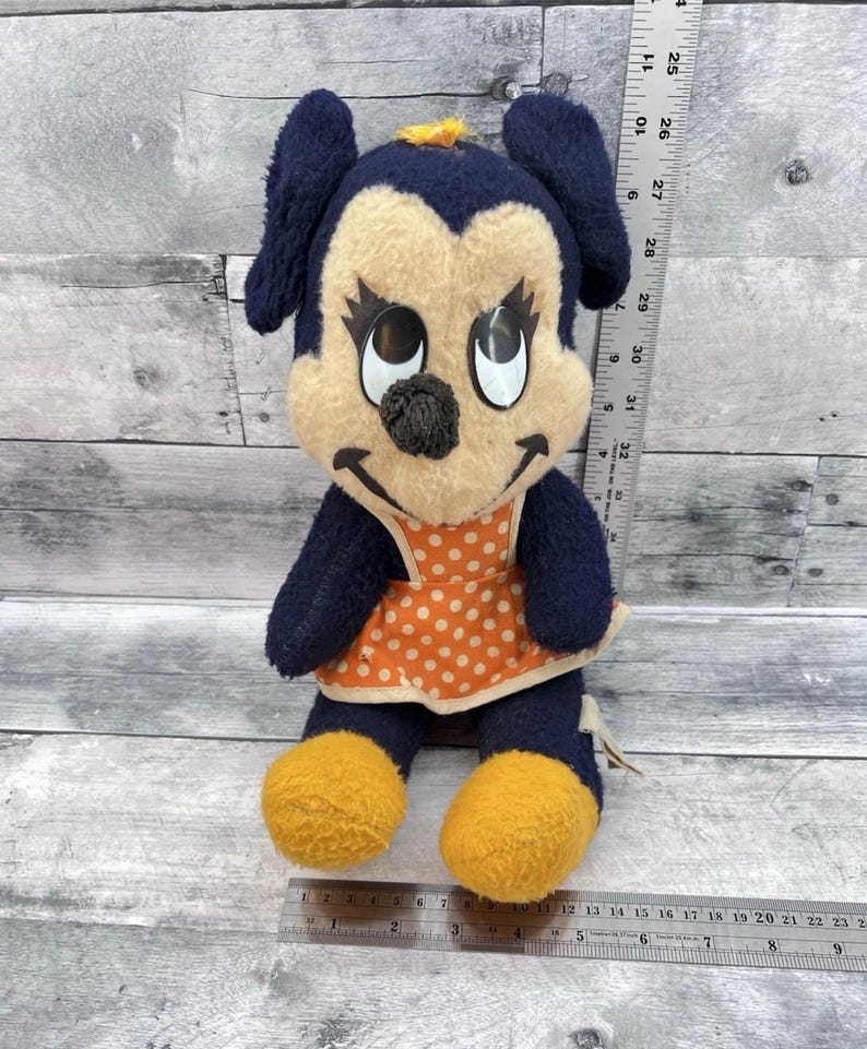 May include: Vintage plush doll featuring a cartoon character with a navy blue head and ears, a tan face, and orange and white polka-dot dress. The doll has yellow feet and a black nose. A ruler is next to the doll.