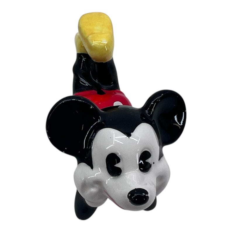 May include: A ceramic Mickey Mouse figurine in a playful pose. The figure features black ears, a white face, and a black nose. Mickey wears red shorts, black shoes, and yellow gloves. The figurine is a collectible item.