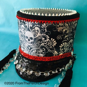 May include: A black and white top hat with a skull design and red trim. The hat is decorated with silver spikes and a chain of clear crystals.