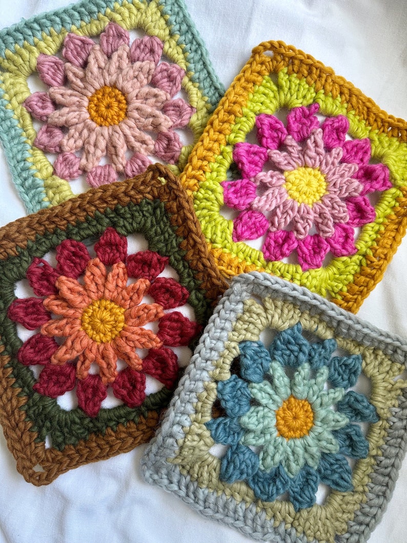 May include: Four crocheted granny squares with different colored flowers in the center. The squares are in shades of blue, green, pink, and orange.