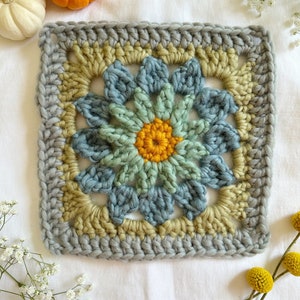 May include: A crocheted square with a flower design in shades of blue, green, and yellow. The flower has a center of yellow yarn and petals in shades of blue and green.