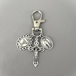 May include: Silver-toned religious keychain featuring a crucifix, a cross, and an oval pendant with a depiction of the Virgin Mary. The keychain has a lobster clasp for easy attachment. The religious-themed accessory is suitable for personal use or as a gift.