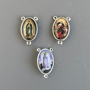 May include: Three silver oval-shaped medallions with images of the Virgin Mary. Each medallion has a silver loop on the top and bottom for attaching to a chain.
