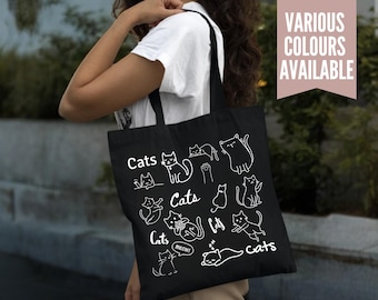 May include: Black tote bag featuring white line drawings of cats in various poses, with the word "Cats" written multiple times. The bag also has the text "VARIOUS COLOURS AVAILABLE" in a pink rectangle.