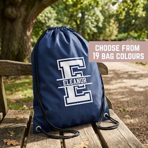 May include: A navy blue drawstring bag featuring a large white letter E with the name ELEANOR printed horizontally across the center. The bag includes black cord straps and text in the upper right corner stating CHOOSE FROM 19 BAG COLOURS.