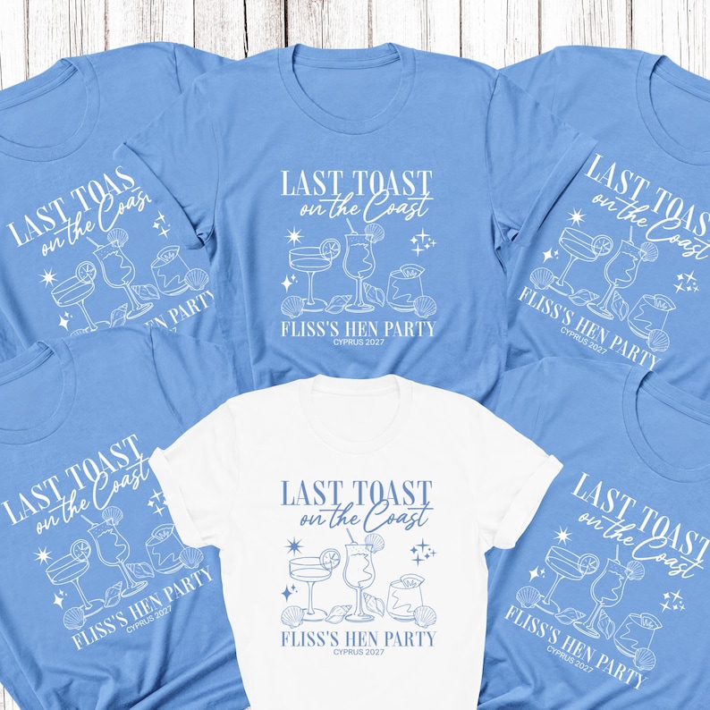 May include: A collection of short-sleeved t-shirts in light blue and white. Each shirt features a white graphic print with the text "LAST TOAST on the Coast" above illustrations of three cocktails, seashells, and stars, with "FLISS'S HEN PARTY CYPRUS 2027" below.