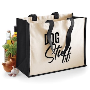 Peut inclure: Un sac fourre-tout en toile crème avec des bordures et des poignées noires. Le sac porte l'inscription "DOG Stuff" en noir. Des oignons, de l'ail et des bouteilles d'huile sont visibles à gauche du sac.