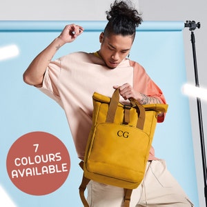May include: A mustard yellow roll-top backpack with adjustable straps and a buckle closure. The backpack has a personalized monogram "CG" on the front.  7 colors available.