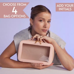 Könnte beinhalten: Eine hellrosa rechteckige Kosmetiktasche mit transparentem Frontpanel und goldenem Reißverschluss. Die Tasche hat einen Griff und die Initialen "JK" auf dem Reißverschluss. Der Text lautet "WÄHLEN SIE AUS 4 TASCHENOPTIONEN" und "FÜGEN SIE IHRE INITIALEN HINZU".