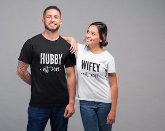 Może przedstawiać: Para w dopasowanych czarno-białych koszulkach z nadrukiem "Hubby - est 2019" i "Wifey - est 2019".