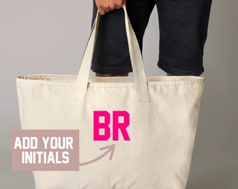 May include: A large, cream-colored tote bag with the hot pink initials "BR" printed on the front. The bag has long handles and the text "ADD YOUR INITIALS" is printed on a pink rectangle.