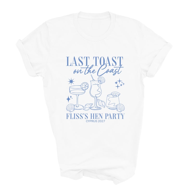 May include: A white short-sleeve t-shirt featuring a blue graphic print with the text "LAST TOAST on the Coast", "FLISS'S HEN PARTY", and "CYPRUS 2027". The design includes illustrations of three cocktail glasses, seashells, and stars.
