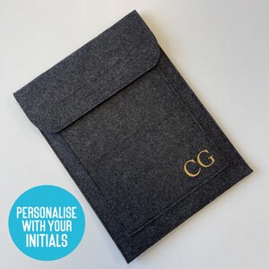 May include: A dark gray felt laptop sleeve with a flap closure. The initials "CG" are in gold on the front. A blue circle in the corner says "Personalise with your Initials".