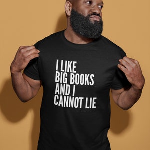 May include: Black t-shirt with the white text "I LIKE BIG BOOKS AND I CANNOT LIE." The shirt is made of a soft material and has short sleeves. The person in the image is wearing the shirt.